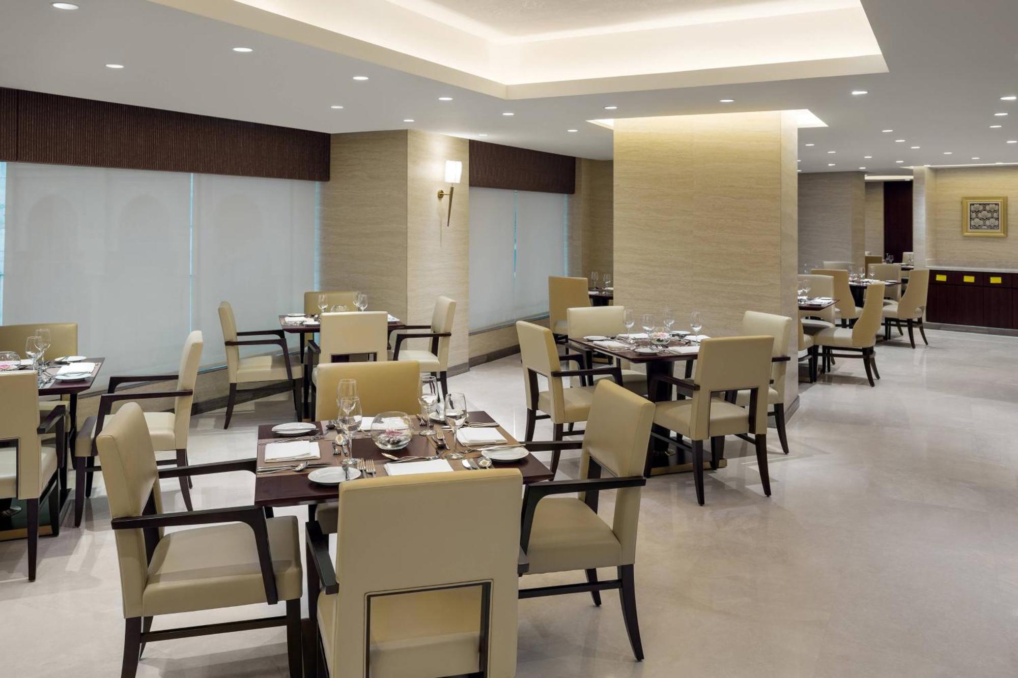 Sheraton Makkah Jabal Al Kaaba Hotel Mekka Exterior foto The photo shows a modern restaurant interior. It features several dining tables, each set with utensils and tableware. The chairs are upholstered in a light fabric, and the overall decor is sleek and minimalistic, with soft lighting from overhead fix